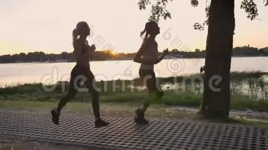 两个年轻漂亮的女人在公园里，在河边的桥上跑步，日落时分，减肥，健身模特慢跑